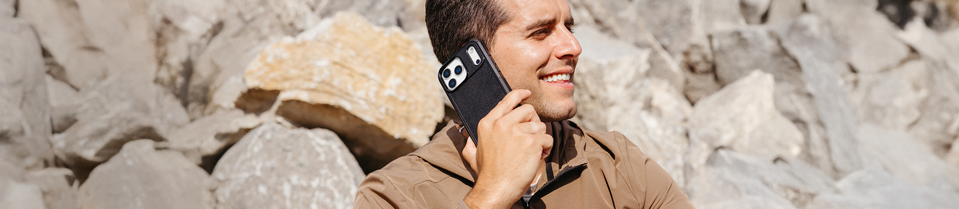 Man holding a smartphone with a case, standing among rocks